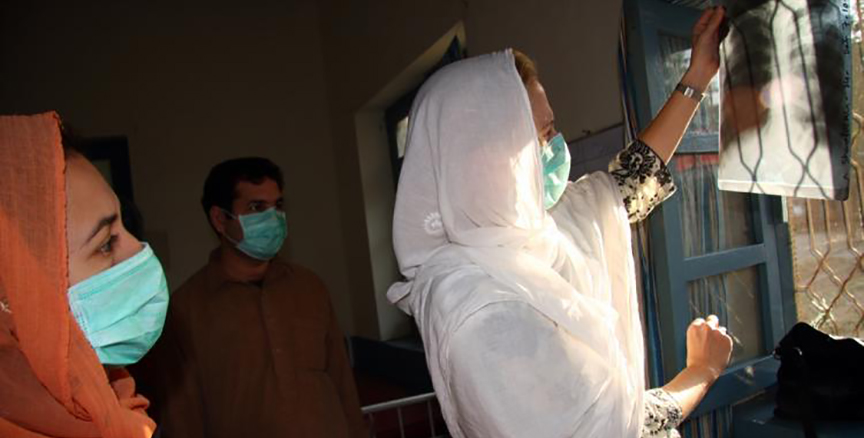 Three people in surgical masks examine an x-ray of a person's lungs.