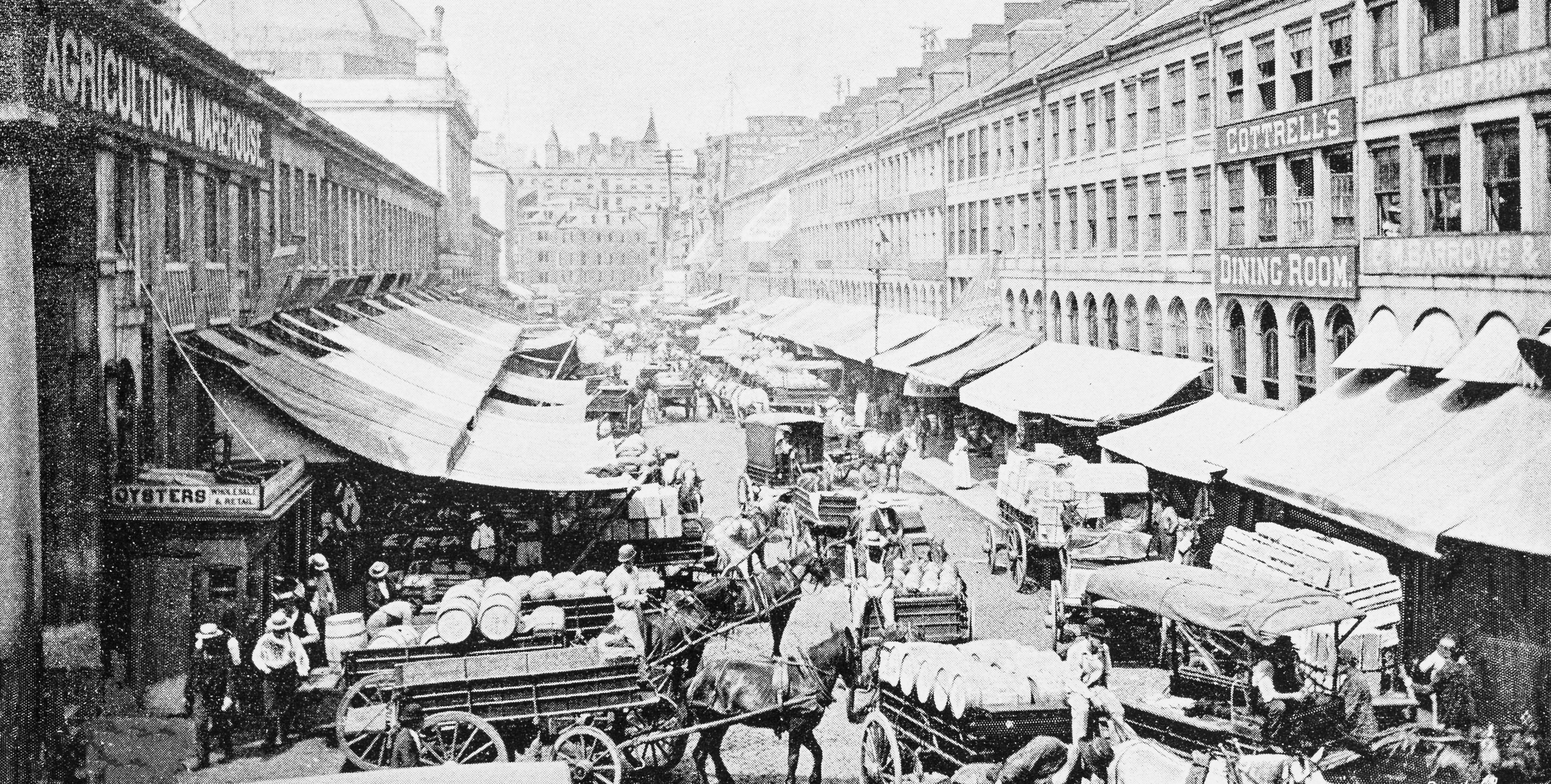 An antique black and white photo of the carts and stalls at Boston's Quincy Market from the 19th century. 