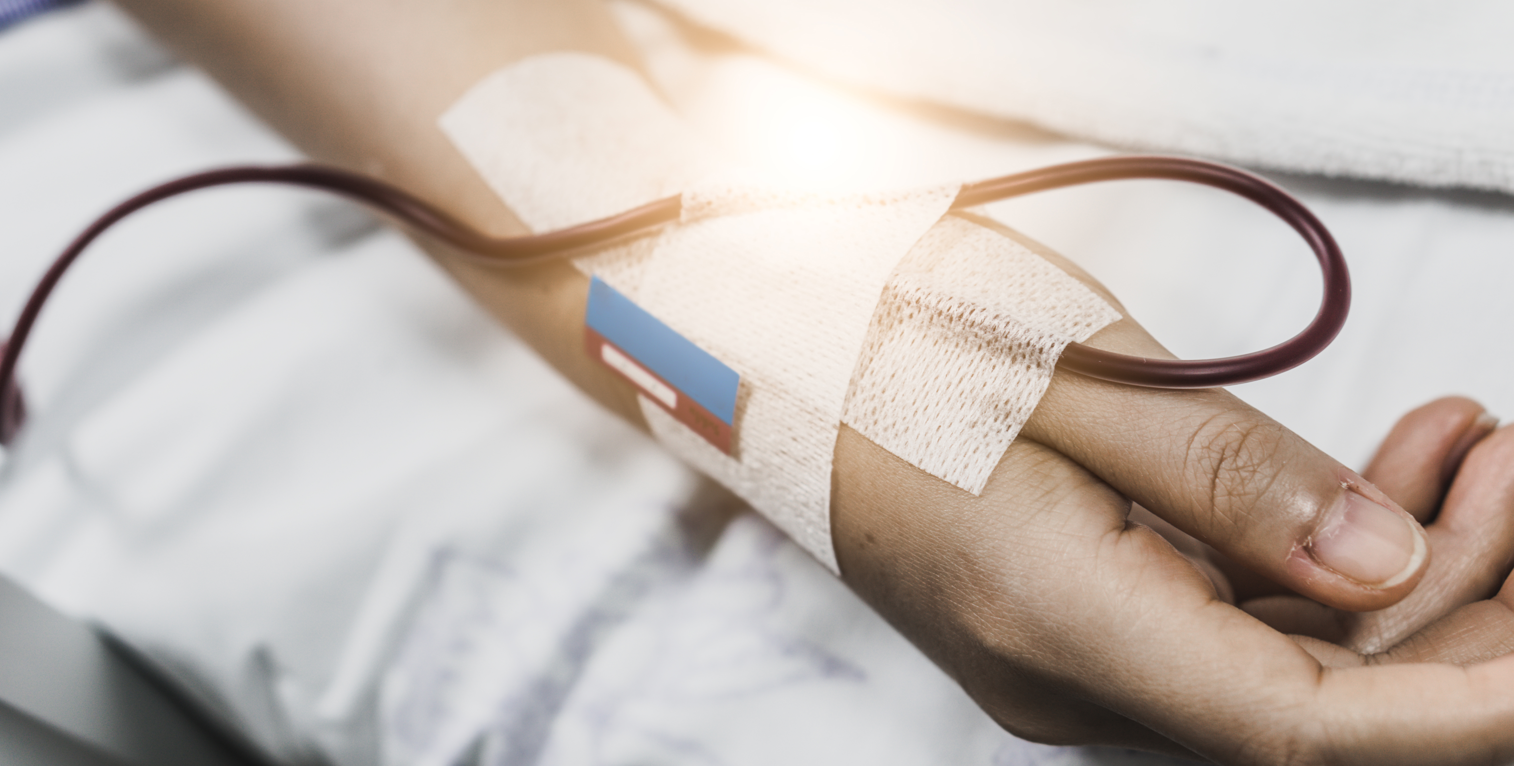 Close-up of a hospital patient's hand with a bandage and an IV tube. 