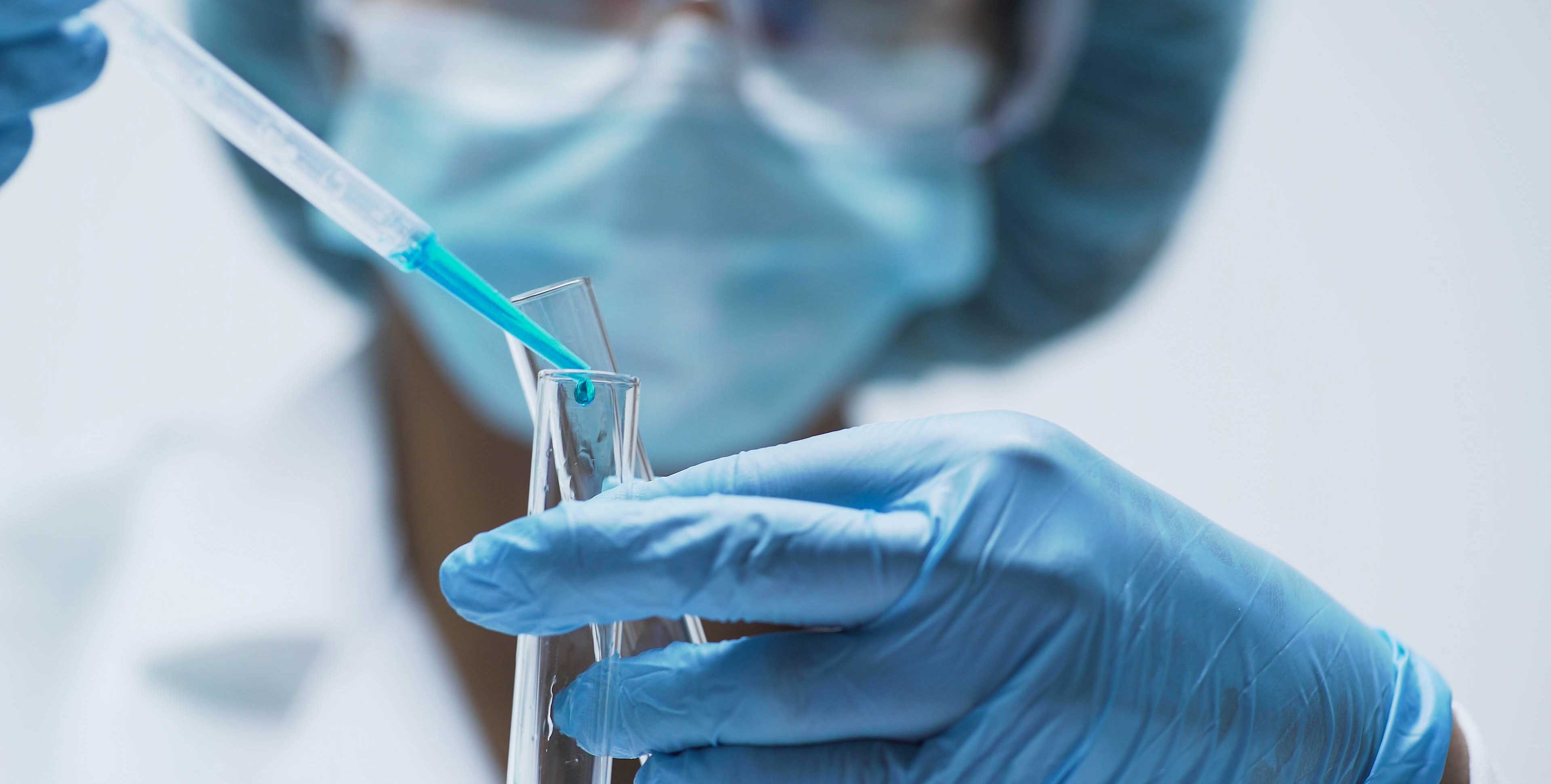 Scientist with mask & gloves pouring liquid into a test tube 