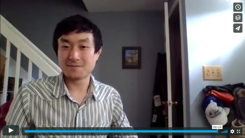 Screen shot of young Asian-American man with bannister and framed photo on wall in background