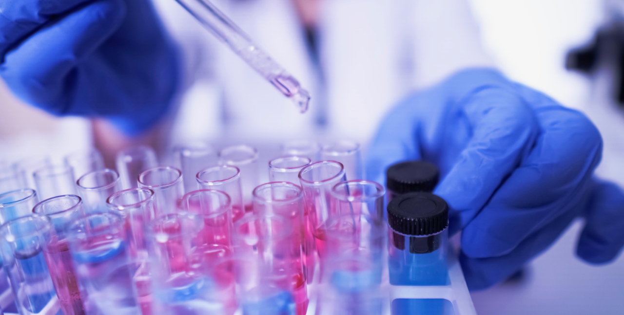 Gloved hands pipette fluid into vials in a rack.	