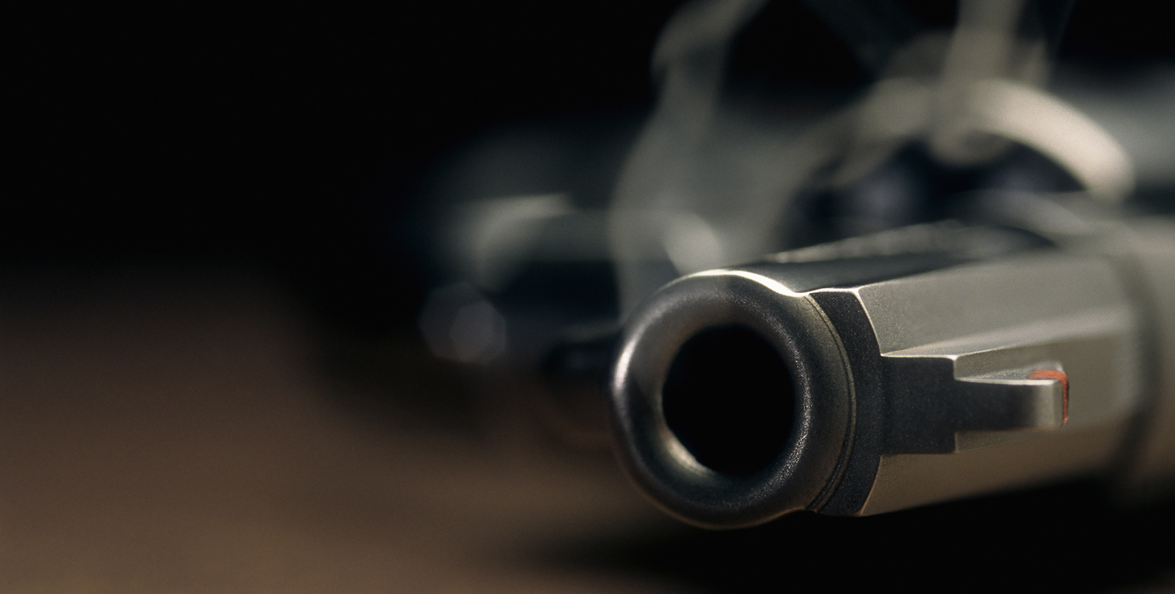 Narrow focus on the barrel of a smoking gun lying on the floor.