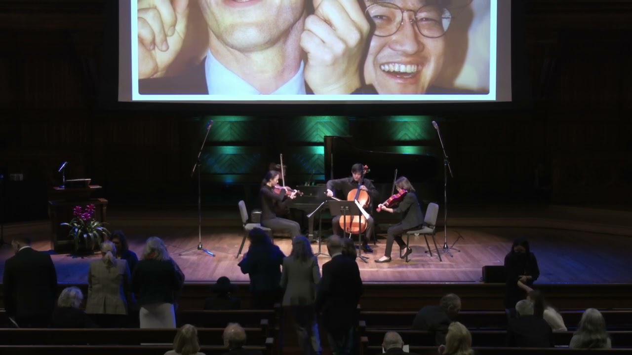 Musicians play on a stage beneath a partial view of a portrait of three faces