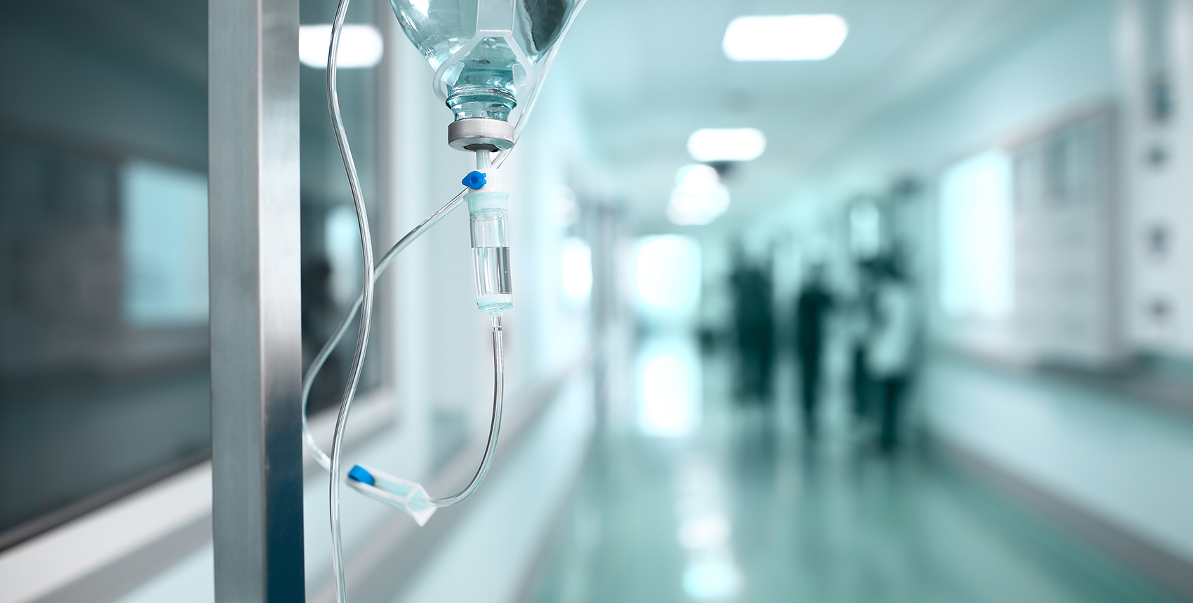 A bag of IV medicine hangs in a lonely hallway.