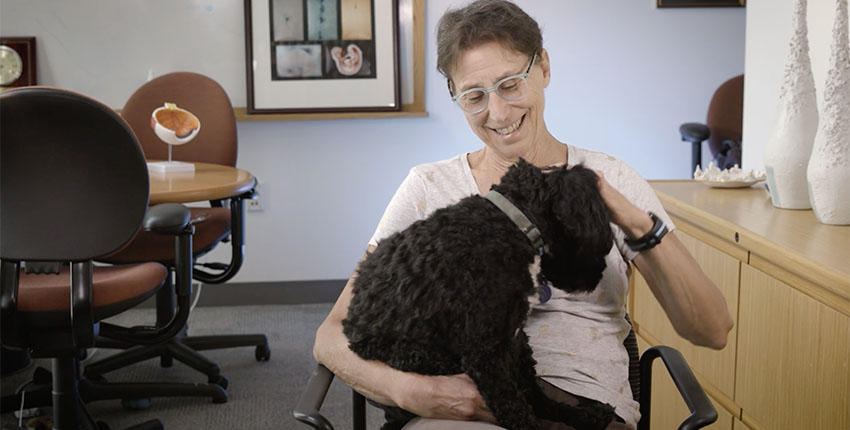 Connie Cepko sits in a chair in her office petting her dog, Stewie