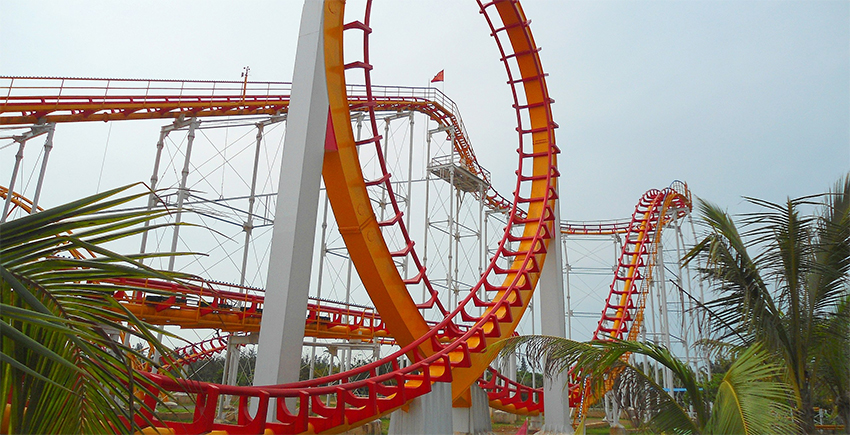 a roller coaster loops around in foreground, then rises and falls in the distance