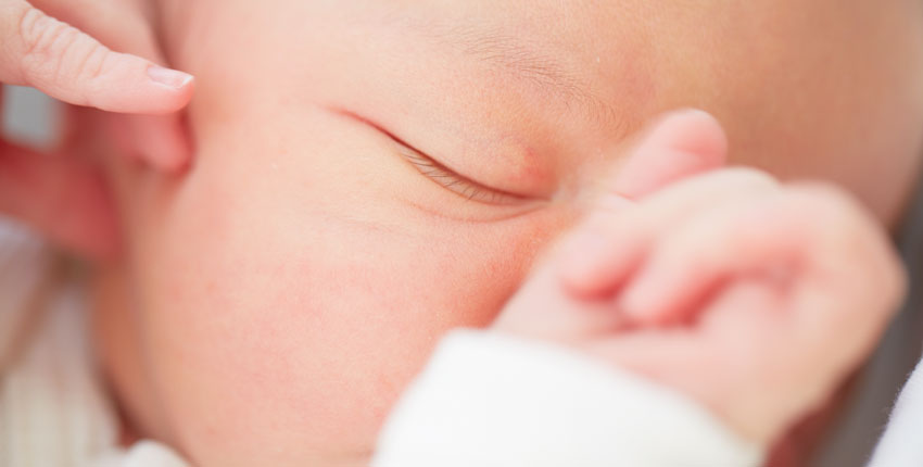 Closeup of a baby's face with one eye closed and hand resting on nose