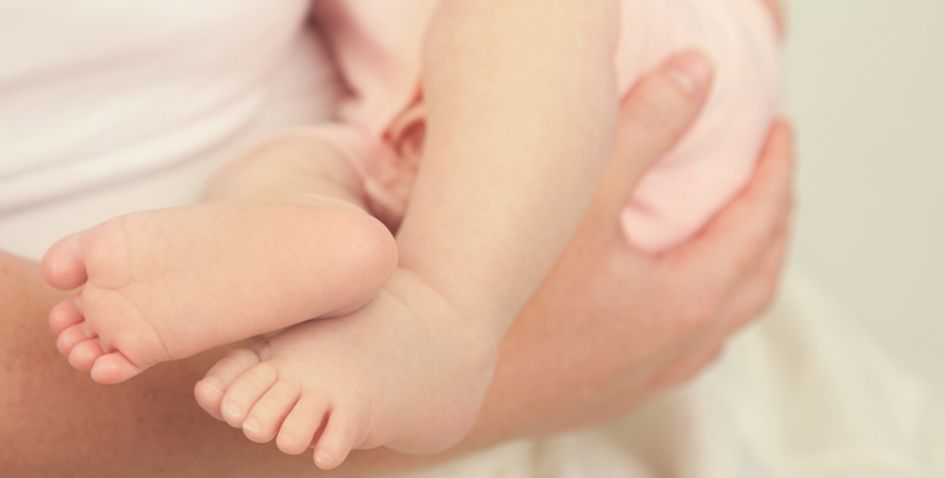 Photo of mothers hands holding an infant, only infant's legs seen