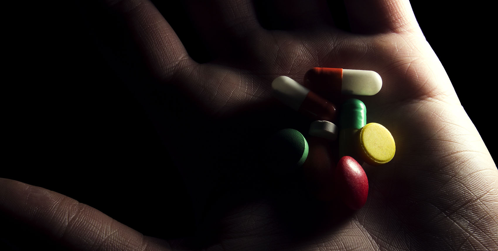 A shadowy hand holds a variety of pills.