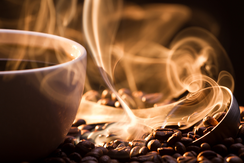 Steaming mug of coffee atop coffee beans