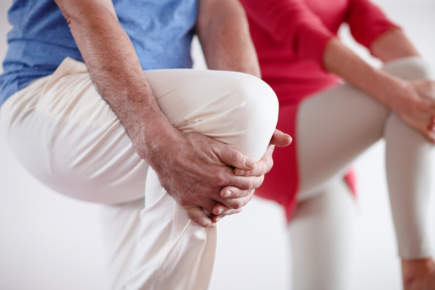 Two people doing yoga balance pose, holding knee and standing on one leg