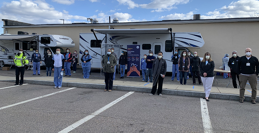 people wearing masks stand 6 feet apart in a parking lot with two RVs in background