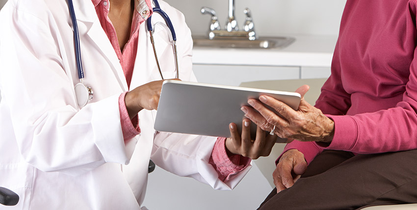 Black female doctor with elderly female patient, both holding and looking at a mobile tablet