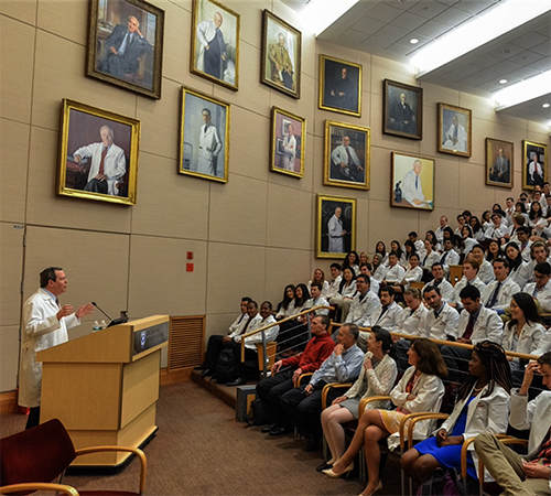 Ed Hundert speaks to students on White Coat Day with portraits hung on the wall in the background