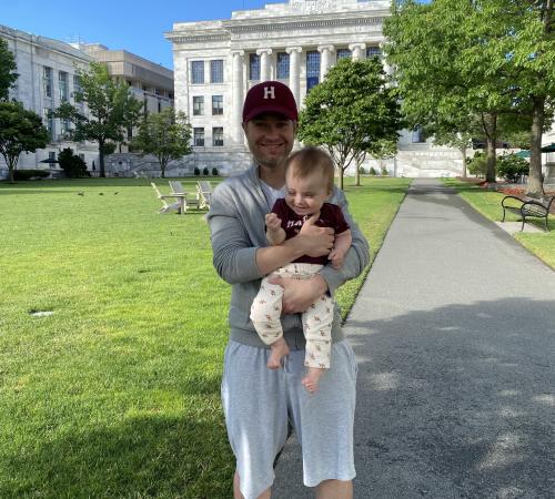 Akerberg holding his son on sunny HMS quad in front of Gordon Hall