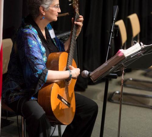 Photo of Marcia Feldman seated playing her guitar