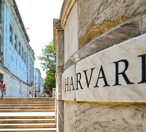 Stone wall says HARVARD in front of the campus Quad