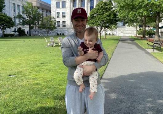 Alex Akerberg holding a baby in front of Gordon Hall