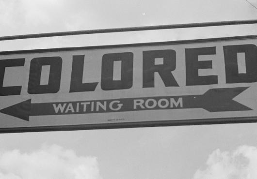 A sign pointing the way to the “colored waiting room” in a 1943 photo of a scene from Rome, Georgia, symbolizes how a legacy of historic racism leads to unequal health care for Black people, Native Americans, and members of other groups that still face discrimination today.