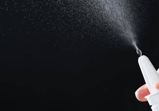 A closeup of a nasal spray nozzle releasing mist into the air