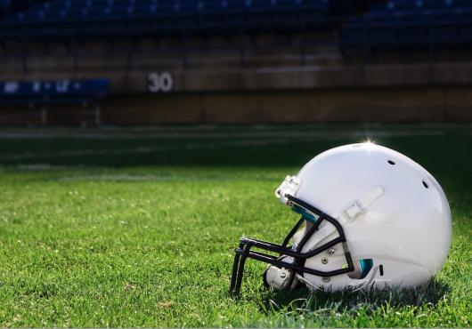 A white football helmet rests on a grass field in a stadium