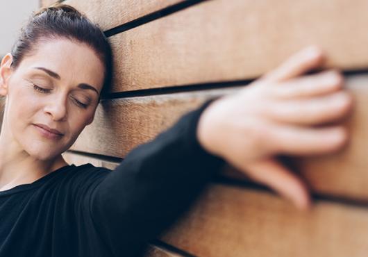 a woman with eyes closed leans her head and her outstretched hand on a wall