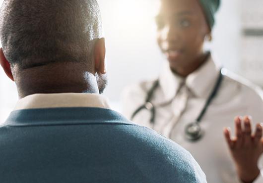 A photograph of a doctor (with face out of focus) talking with her patient, who has his back to the camera.