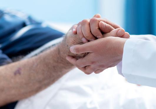 Close up of doctor in white coat holding the hand of an elderly patient