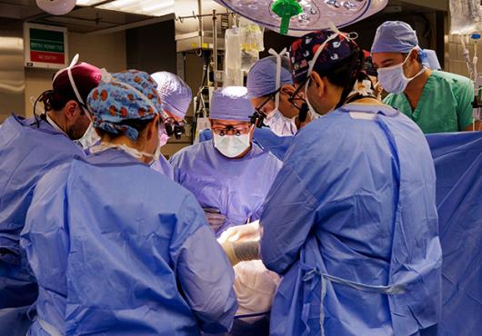 Eight people in surgical garb cluster around an operating table