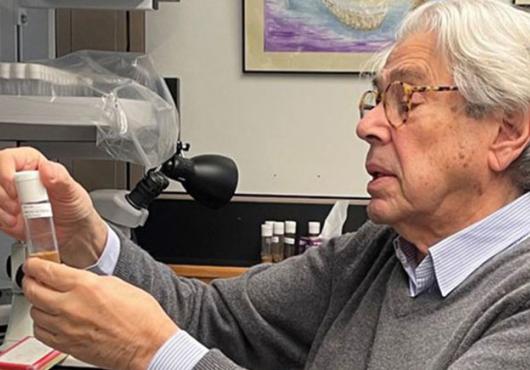A professor sitting at a lab bench looking at a small plastic container