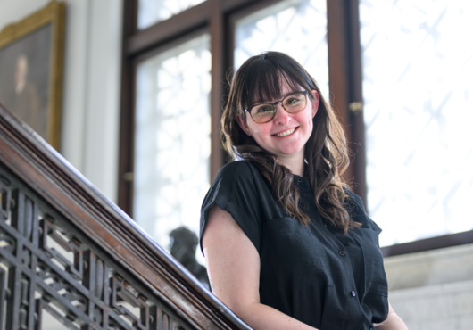 A woman leans on a banister and smiles at the camera
