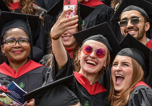 A woman holds up a cell phone to take a selfie with several other people.