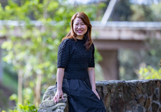 A woman sits on a stone wall and smiles at the camera