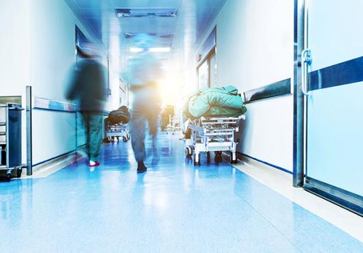 A backlit photo showing health care providers walking up a hallway away from the camera. The unsettling lighting and motion blur convey a sense of unease.