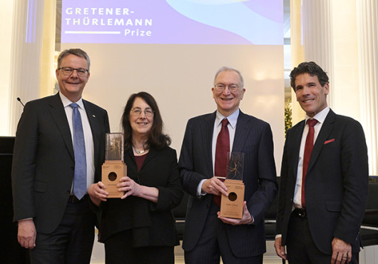 Sharpe and Freeman hold their awards, flanked by Shaepman and Dall'O. They stand in front of a screen with the prize name on it.
