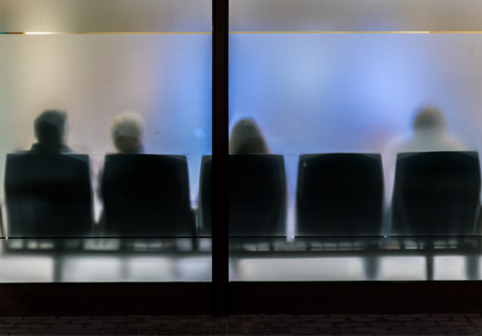 An abstract photograph of a waiting room with frosted glass and people sitting in chairs