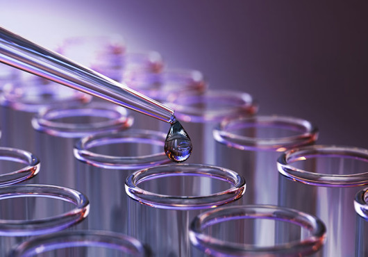 A drop of colorful fluid flows from a pipette into one of many vials in an array.