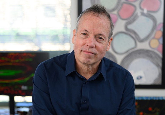 A man in a navy-blue shirt sitting on a table with his arms crossed