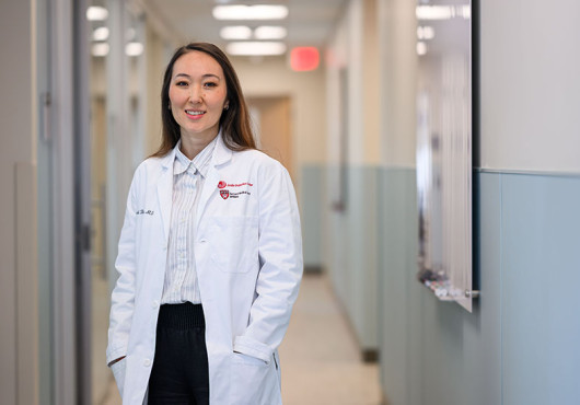 A woman in an HMS/Joslin white coat stands in a hallway.
