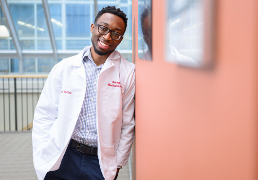 Leonard Nettey leans on a wall. He is wearing a white coat.