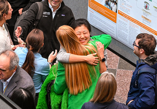 Two women hug in front of a research poster with six others nearby