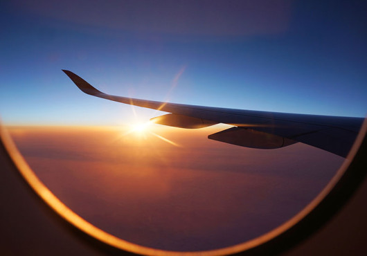 View out an airplane window of a plane’s wing at sunset.