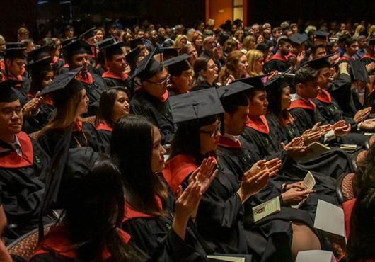 Audience shot of graduates in black and red regalia