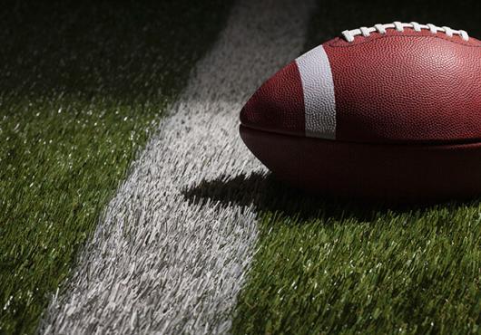 A football lays on the grass in front of a white line.