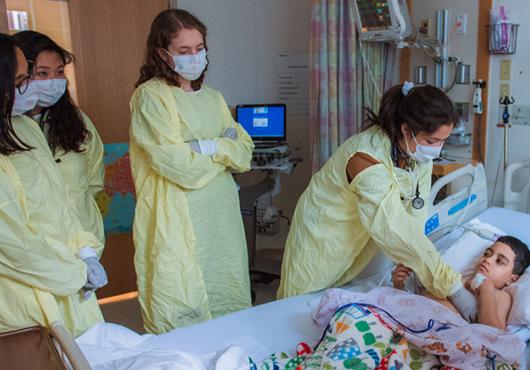Photo of several HMS students in protective gowns examining a pediatric patient