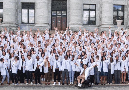Entering students in white coats on steps of Gordon Hall raising arms and shouting with joy