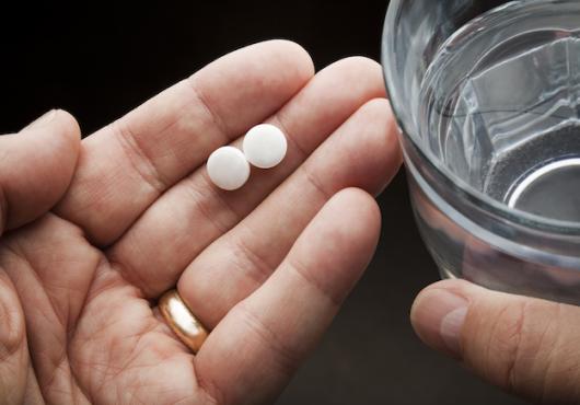 Hand holding aspirins and a glass of water 