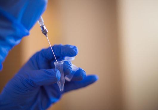 A gloved hand holding small vial and a second gloved hand holding a syringe