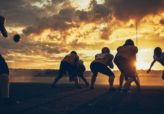 Photo of athletes playing football on a field at sunset